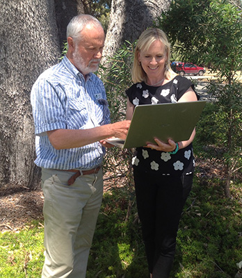 Two people underneath a tree, looking at a laptop.