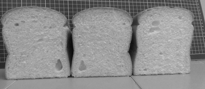 Three different loaves of bread, sliced vertically with the open end showing.